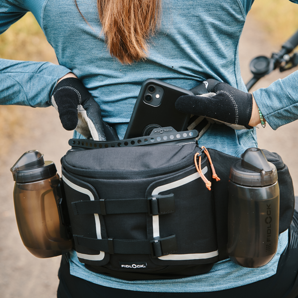 Fidlock Hip Belt + Double Bottle Base Hip pack with TWIST magnetic & mechanically latching water bottles worn by mountain biker putting phone in waterproof compartment