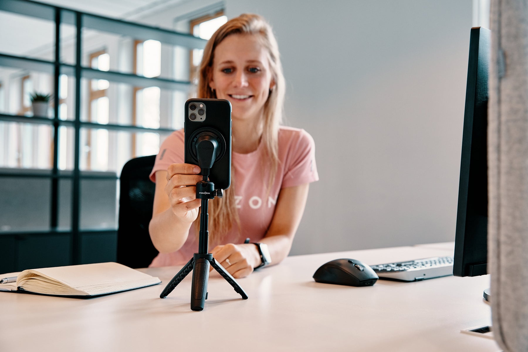 Fidlock VACUUM phone mounting system used with a tripod by a woman for video conferencing