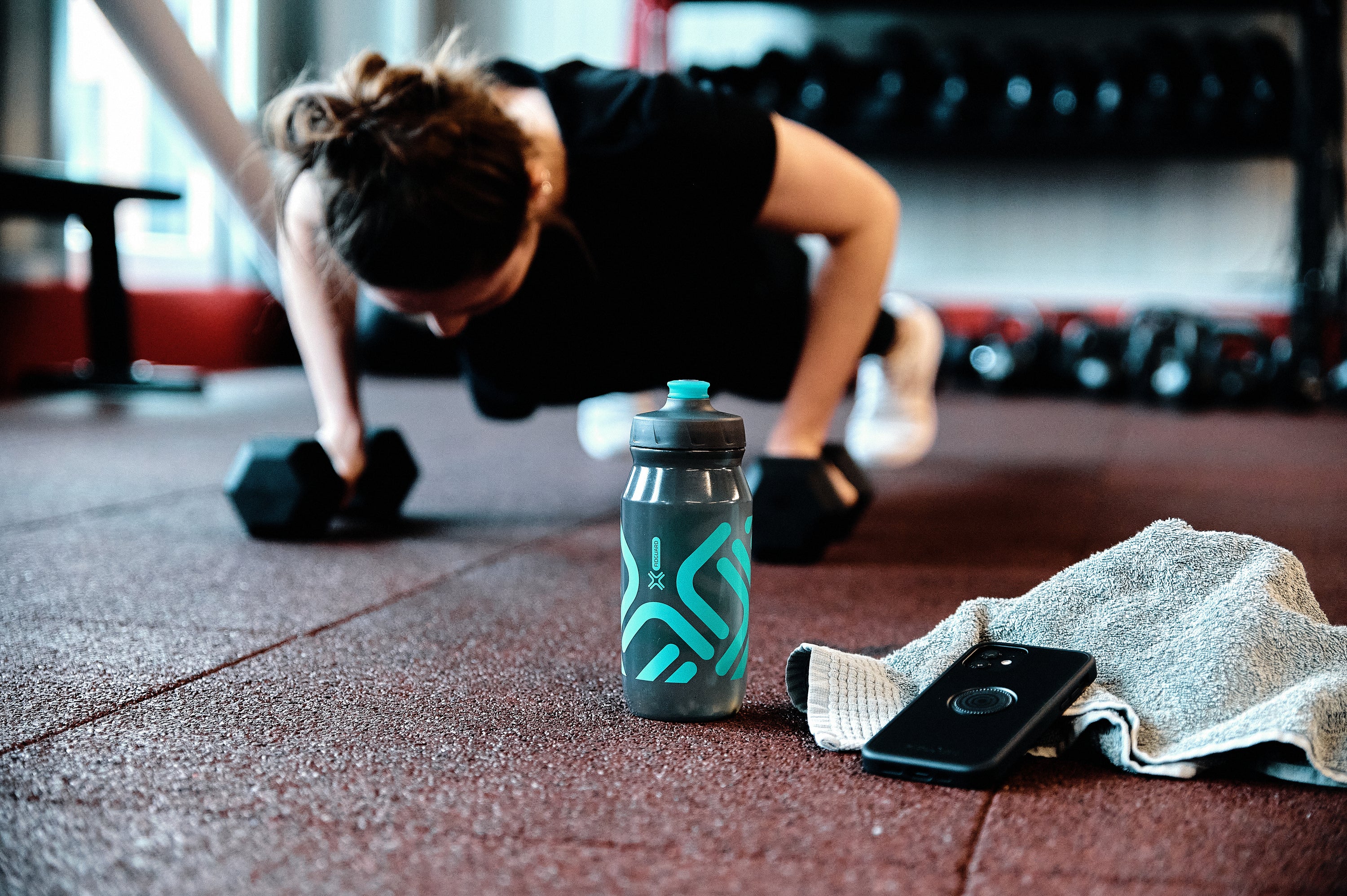 Fidlock Fidguard antibacterial water bottle on gym floor with woman doing barbell pushups