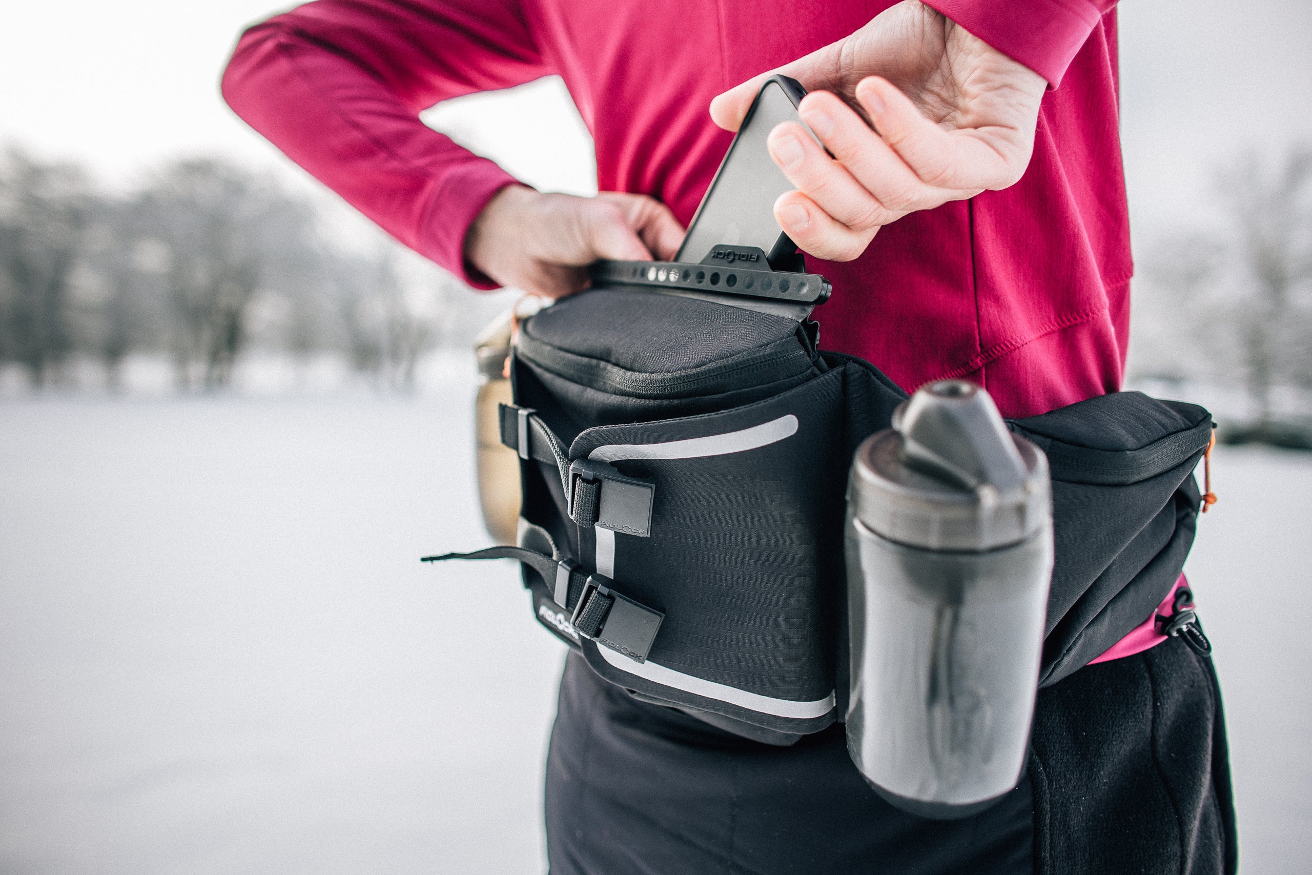 Woman putting cell phone into the Fidlock hip pack she is wearing in a winter landscape