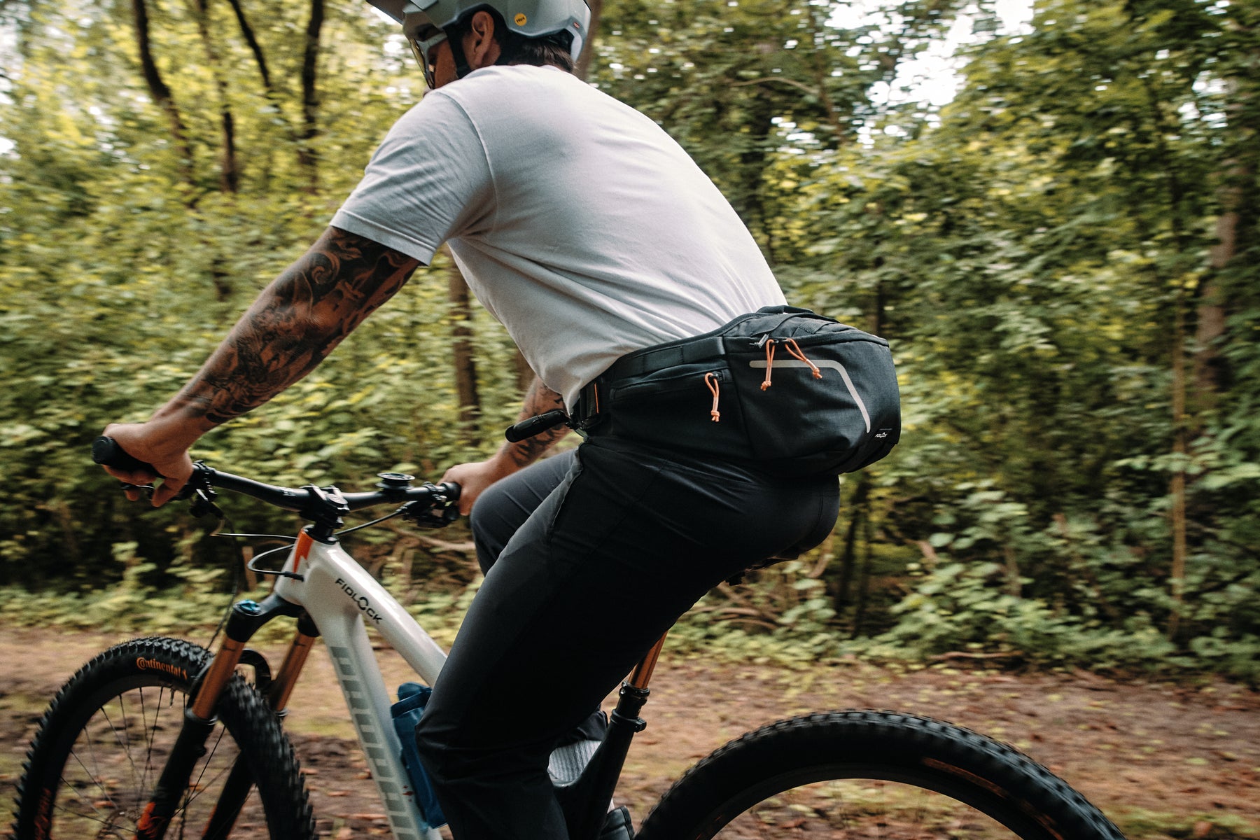 Mountain biker riding through forest wearing Fidlock hip pack with hydration bladder