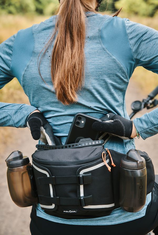 Mountain biker placing her cell phone inside waterproof compartment of Fidlock hip pack with two magnetically attached water bottles